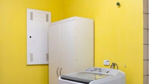 Una sala de bugaderia amb una rentadora, una assecadora i un armari blanc davant d'una paret groga.