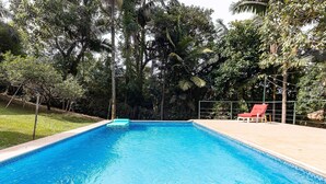 Une piscine rectangulaire dont les bords sont recouverts de carreaux, entourée d’une clôture et d’arbres.