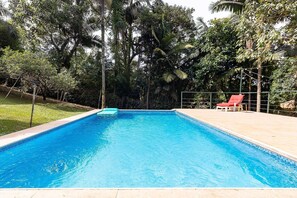 Una piscina rectangular amb vora enrajolada, envoltada per una tanca i arbres.