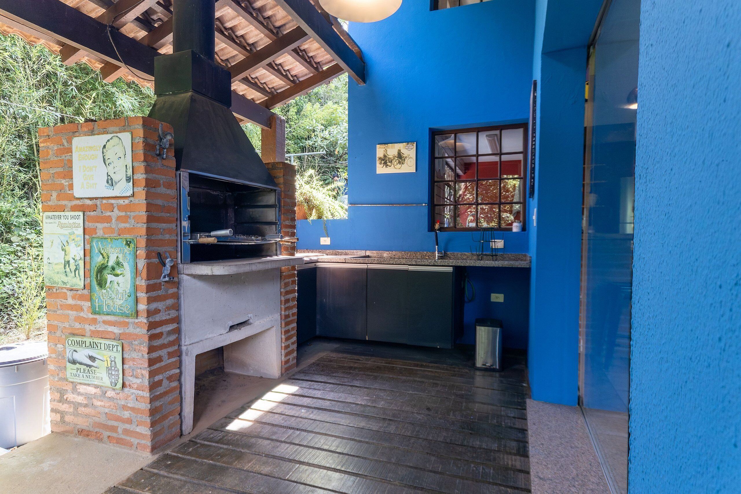 An outdoor kitchen with a brick oven, a window, and a blue wall.