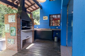 An outdoor kitchen with a brick oven, a window, and a blue wall. - Casa ampla com piscina e churrasqueira  (Carapicuíba)