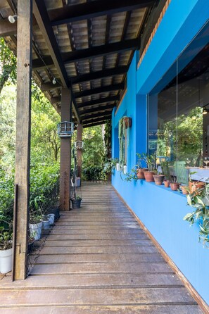A covered wooden deck with potted plants and a blue wall. - Casa ampla com piscina e churrasqueira  (Carapicuíba)