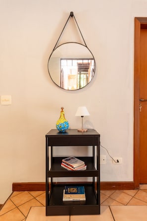 A black console table with a mirror above it, a vase, a lamp, and books. - Casa ampla com piscina e churrasqueira (Carapicuíba)
