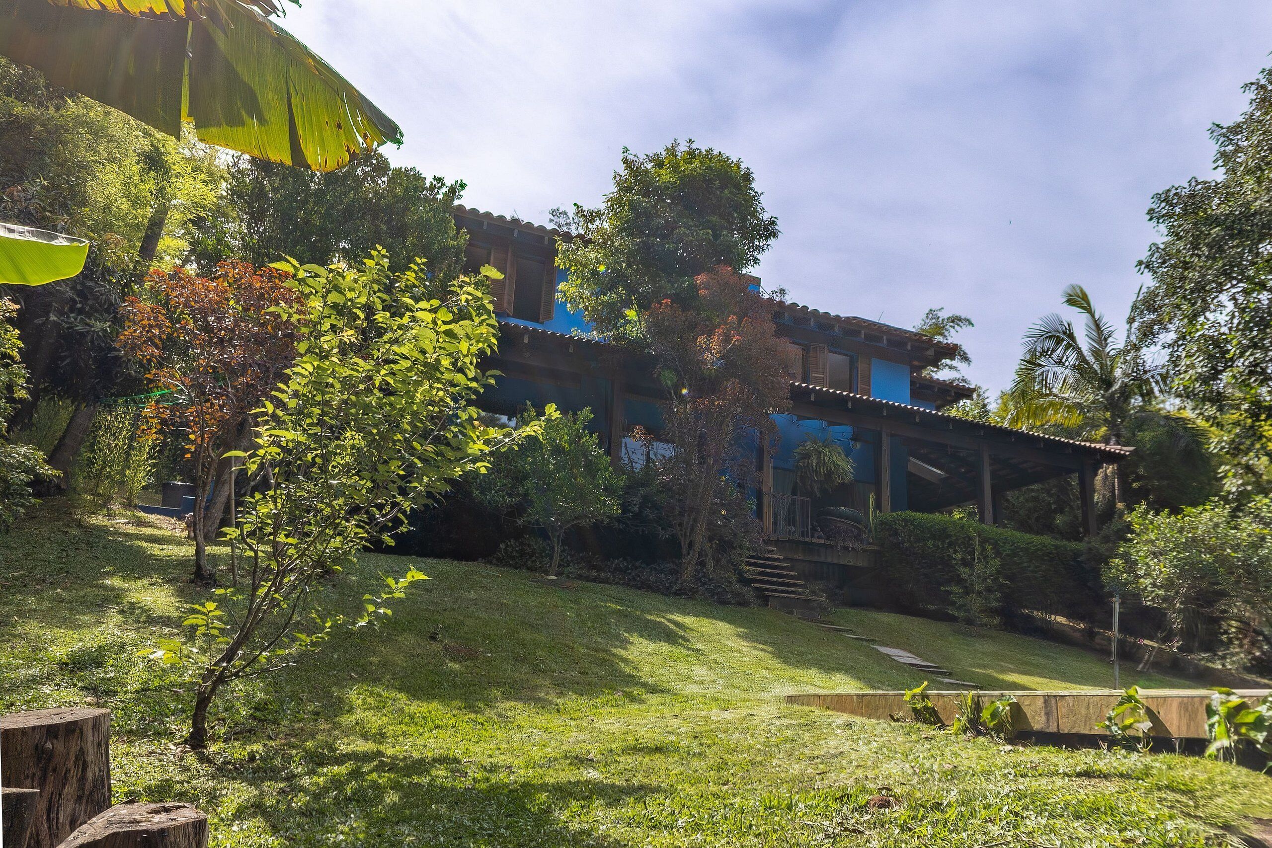 A house with a blue roof, surrounded by lush greenery and a small garden.