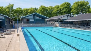 En swimmingpool med tydelige baner, tilstødende liggestole og et overdækket tilskuerområde.
