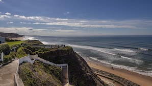 Blick auf die Küste mit einer Treppe, die zu einem Strand führt, einem Holzzaun und einem klaren Himmel.