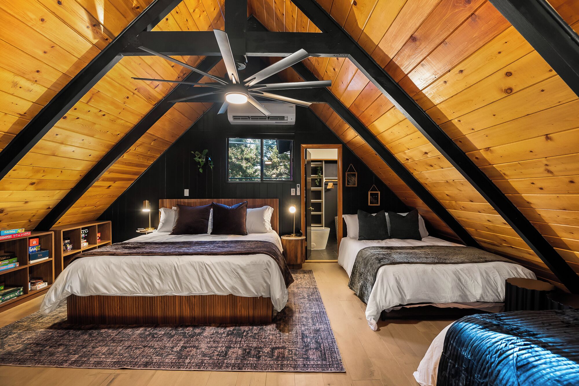 Een knus slaapkamer op zolder met twee bedden, een plafondventilator en een groot raam.