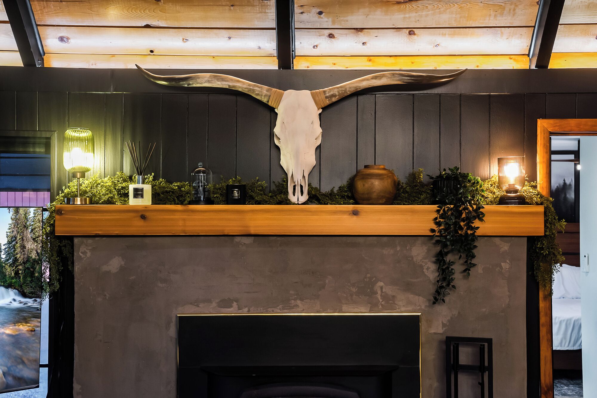 Een haard met een groot dierenschedel erboven, omringd door begroeiing en decoratieve objecten.