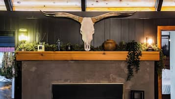 Een haard met een groot dierenschedel erboven, omringd door begroeiing en decoratieve objecten.