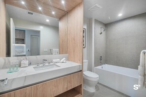 Ein modernes Badezimmer mit Marmorwaschbecken, Holzschränken, einer Toilette und einer Badewanne.