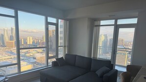 Una sala de estar moderna con un sofá modular, una mesa de comedor y ventanas amplias que ofrecen vistas de la ciudad.