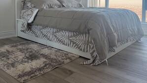 Un dormitorio con una cama grande, vistas de la ciudad a través de la ventana y un tapete mullido en el suelo.