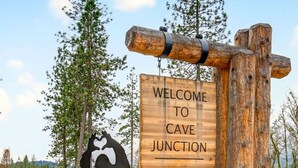 A wooden sign with the text "WELCOME TO CAVE JUNCTION" and a silhouette of a person climbing a rock. - Redwoods Stopover- Near Hiking, Pet Friendly (Cave Junction)