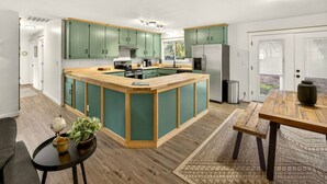 A modern kitchen with green cabinets, a wooden island, and a dining area with a table and bench. - Redwoods Stopover- Near Hiking, Pet Friendly (Cave Junction)