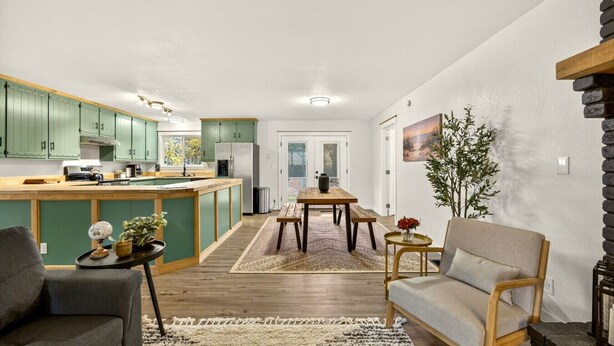 A modern kitchen with green cabinets, a wooden dining table, and a cozy seating area with a sofa and armchair. - Redwoods Stopover- Near Hiking, Pet Friendly (Cave Junction)