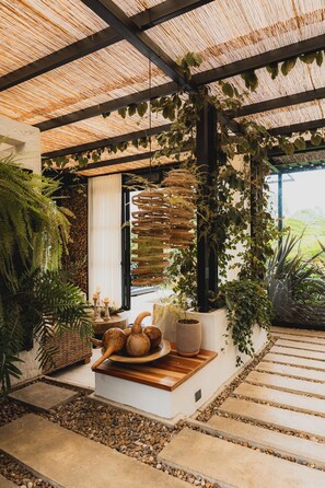 A covered outdoor area with a stone pathway, potted plants, and a wooden table with decorative items.