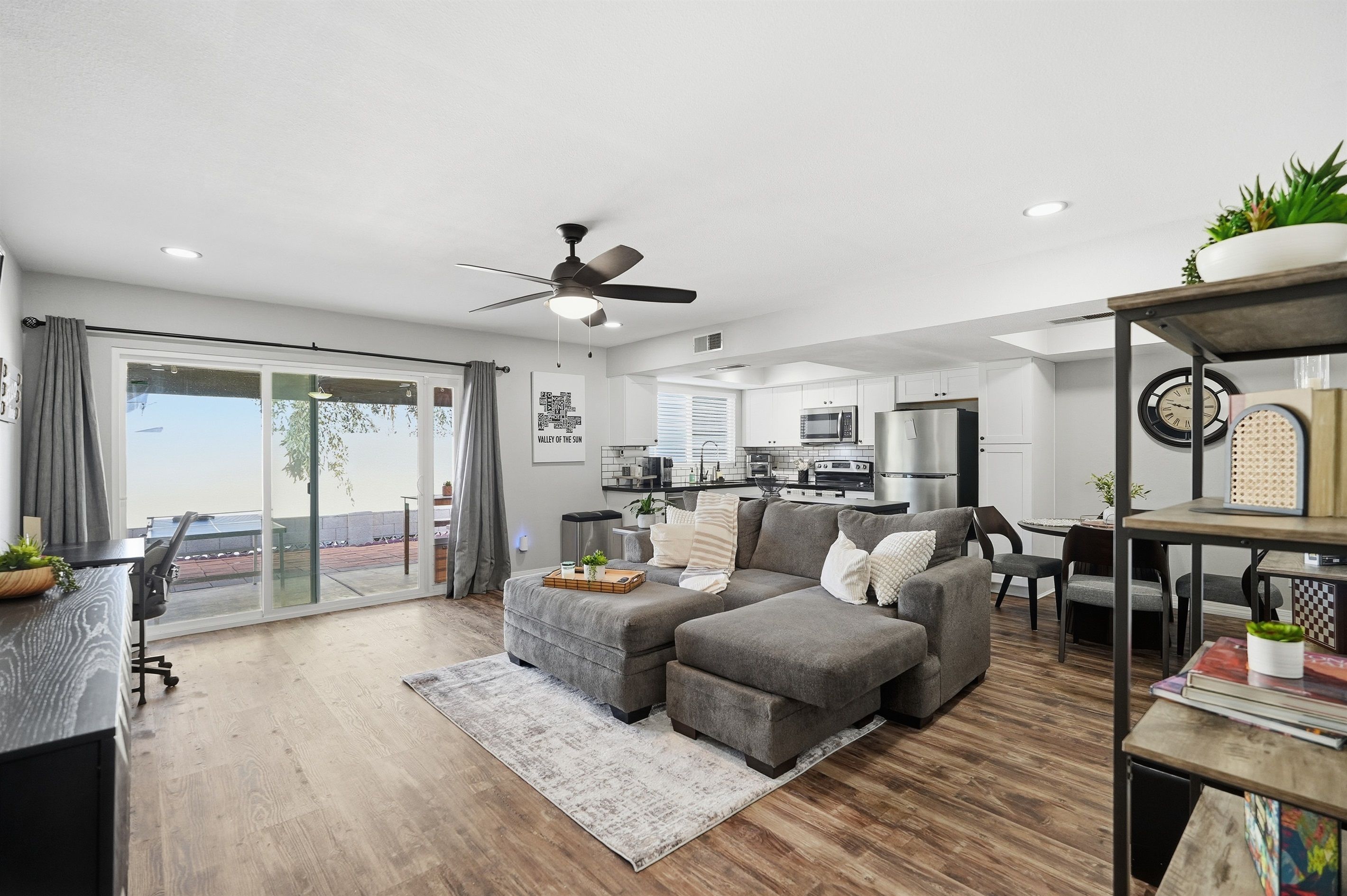 A modern living room with a grey sectional sofa, a ceiling fan, and a dining area with a small table and chairs.