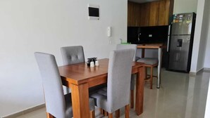 Ein Essbereich mit einem Holztisch und vier grau gepolsterten Stühlen. Im Hintergrund ist eine Küche mit Holzschränken und einem Edelstahlkühlschrank zu sehen.