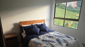 Ein Schlafzimmer mit einem Bett, einem Nachttisch und einem Fenster mit Blick auf eine Baustelle.