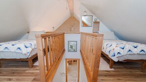 Quarto com duas camas, grades de madeira, piso de madeira e uma pequena porta ao centro.