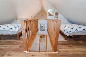 A bedroom with two beds, wooden railings, a wooden floor, and a small door in the center.