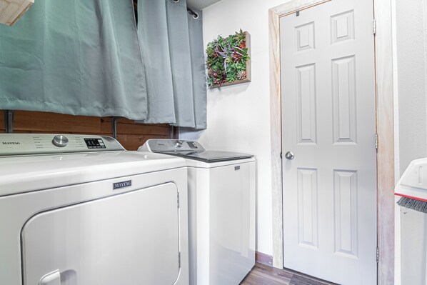 A laundry area with a Maytag washer and dryer, a grey curtain, and a door with a small plant decoration.