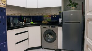 Une cuisine compacte équipée d’un lave-linge, d’un réfrigérateur et d’un panneau indiquant la disponibilité de produits frais.