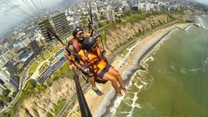 A person bungee jumping with safety harnesses, overlooking a coastal cityscape with buildings and a beach. - Modern 2BR Apt for 8 +Parking | Central Miraflores (Miraflores)