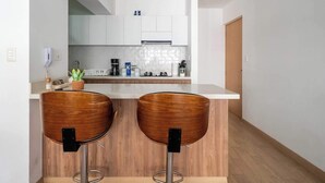 A modern kitchen with white cabinets, a wooden countertop, and two bar stools. - Modern 2BR Apt for 8 +Parking | Central Miraflores (Miraflores)