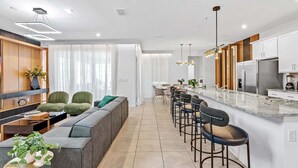Una cocina moderna con una isla central, taburetes de bar y una zona de estar con sofá y sillones.
