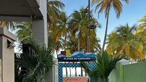 A pathway leading to a sign reading "Playas de Carolina" with palm trees and a clear sky in the background. - Isla Verde Beach Studio with Pool & Parking! A2 (Carolina)