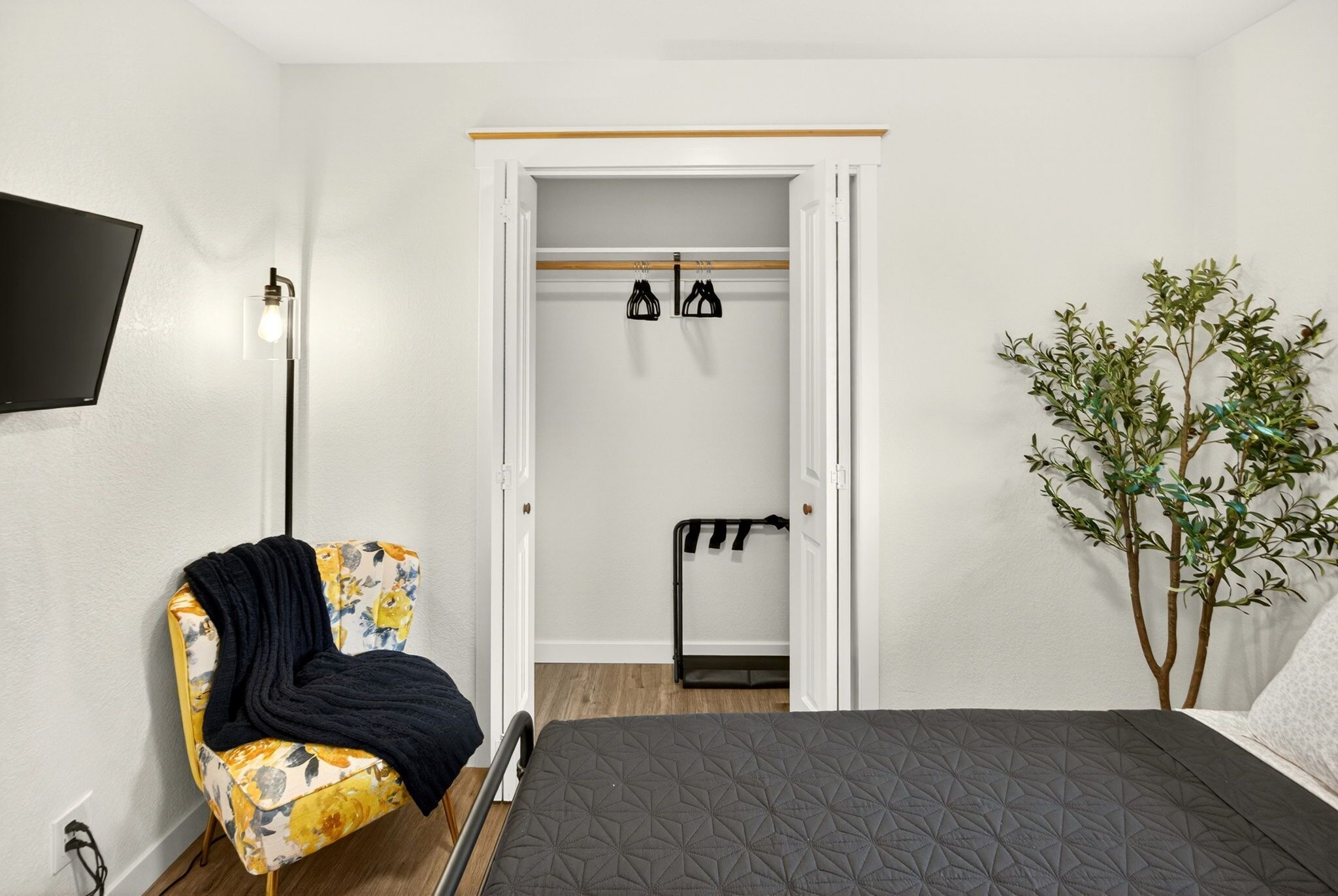 A bedroom with a bed, a chair, a coat rack, and a plant.