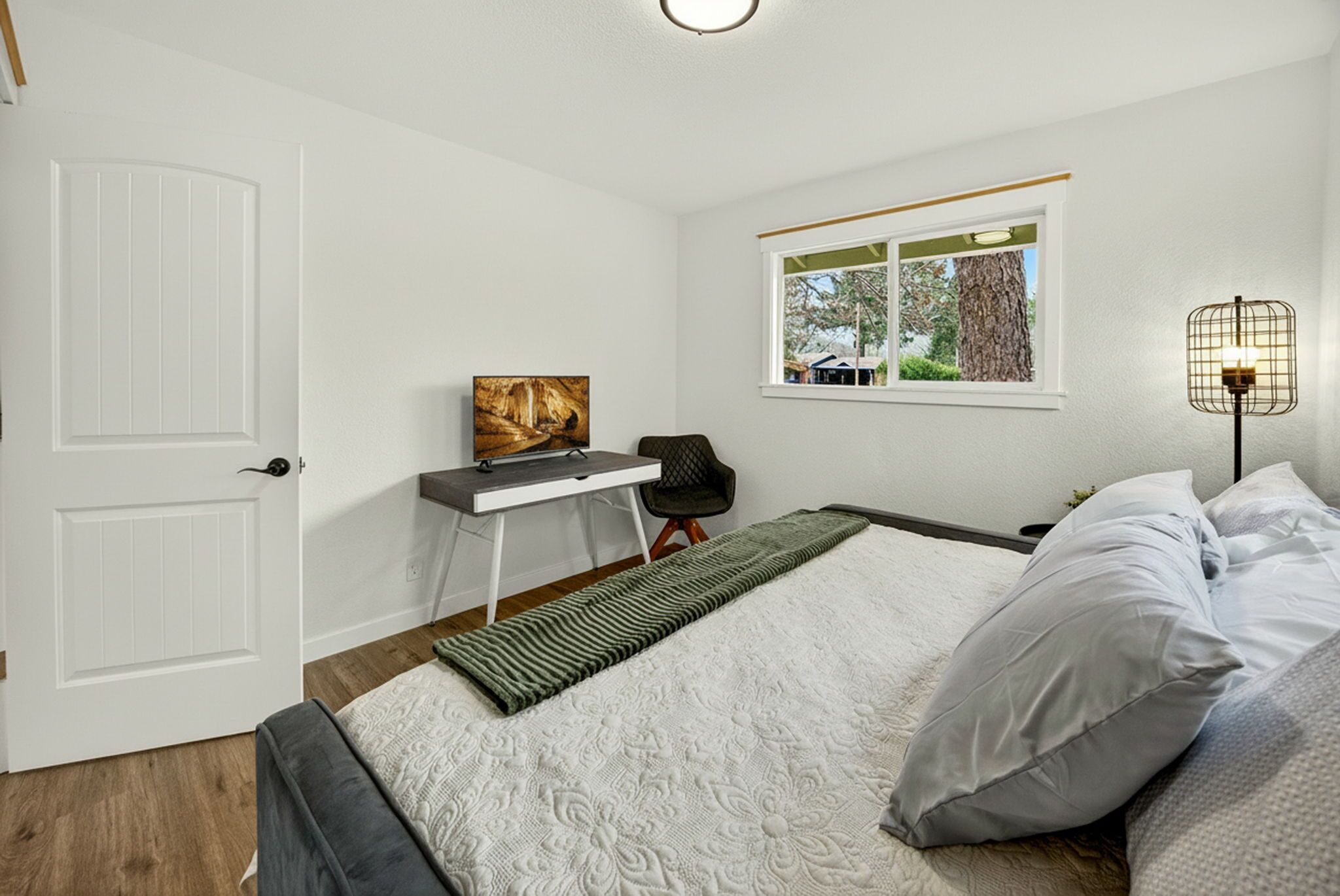 Quarto com cama, escrivaninha, cadeira, janela e luminária.