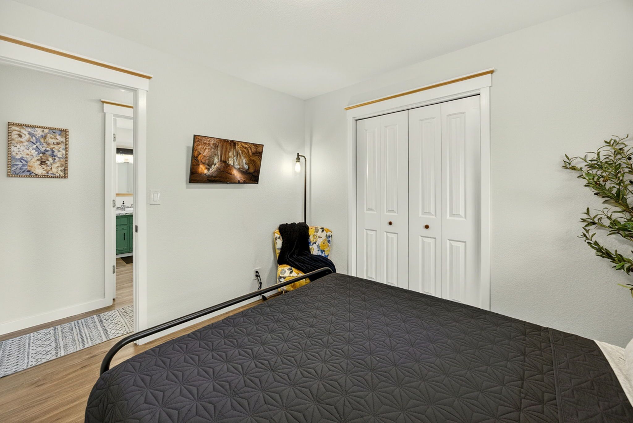 A bedroom with a bed, a chair, a painting, and a wardrobe.