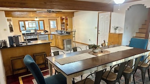 Un comedor con una larga mesa de madera, varias sillas y una cocina al fondo.