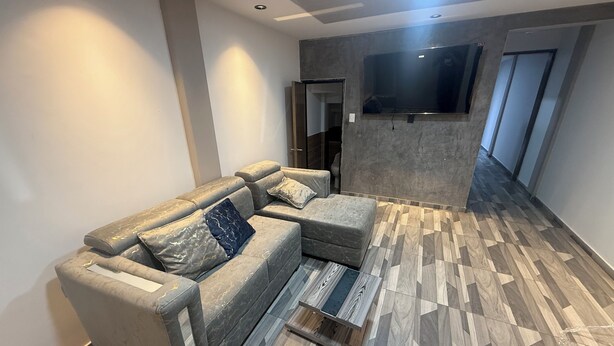 Ein modernes Wohnzimmer mit einem Ecksofa, einem flachbildfernseher an der Wand und einem Fischgrätparkettboden.