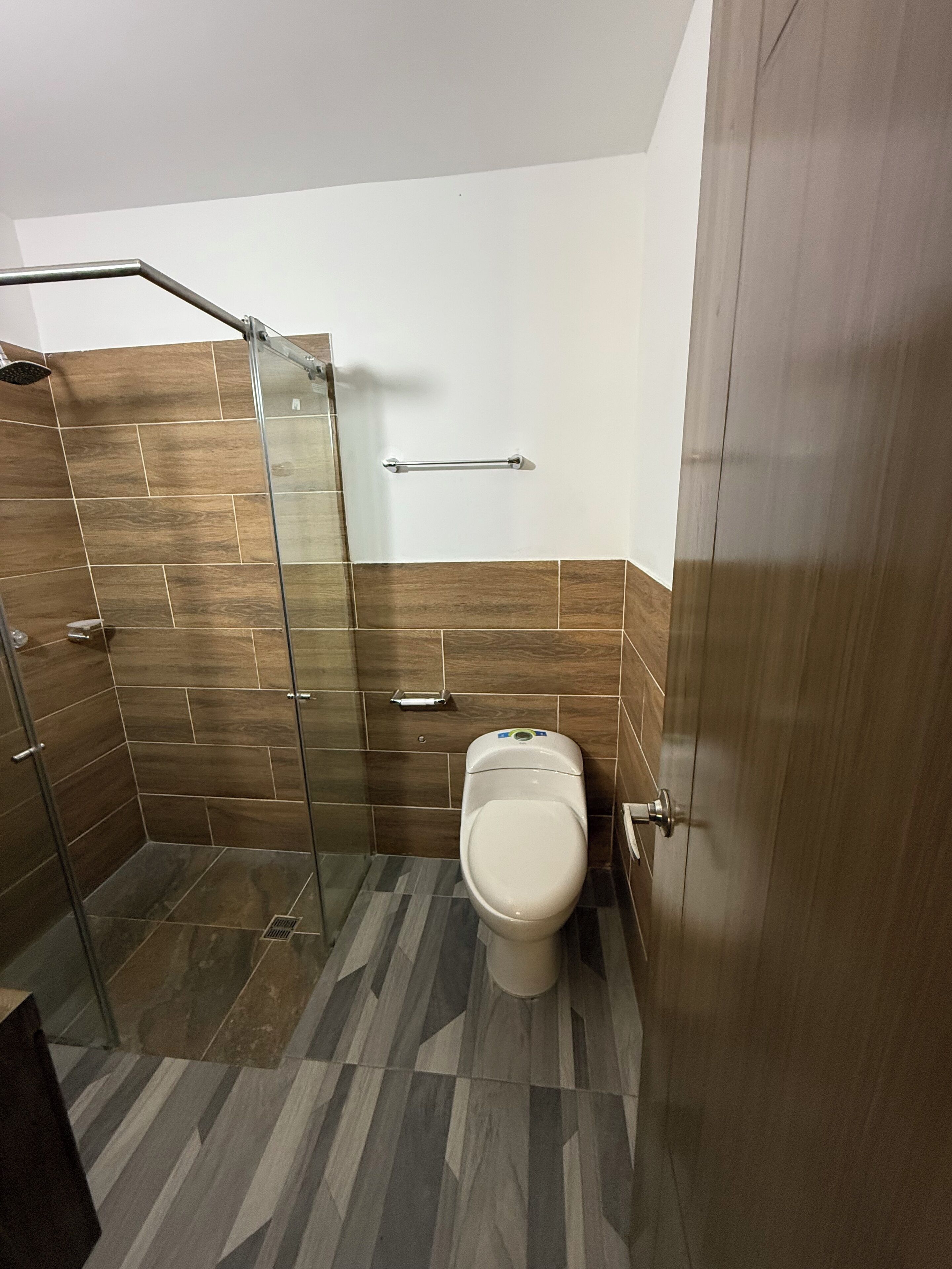 A compact bathroom with a glass shower enclosure, a toilet, and a towel rack.