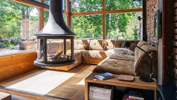 Ein gemütliches Wohnzimmer mit einem großen Fenster, einem Kamin aus Stein, einer gepolsterten Couch und einem Couchtisch aus Holz.