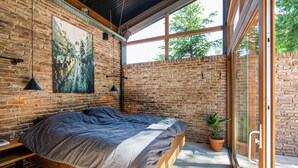 Ein modernes Schlafzimmer mit Backsteinwand, großem Fenster und einem Bett mit Holzrahmen.