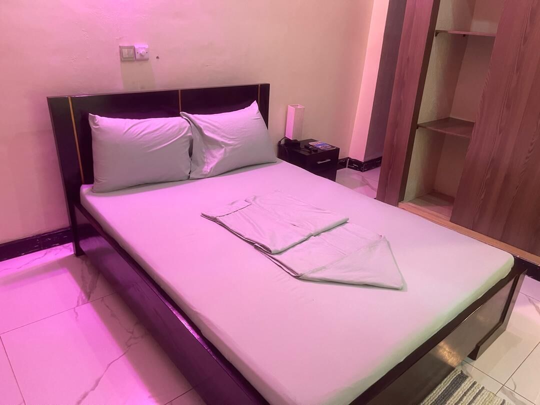 A neatly made bed with pillows, a bedside table with a lamp, and a wooden wardrobe.