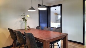 Un comedor con una mesa de madera, seis sillas, dos lámparas colgantes y un florero con una flor.
