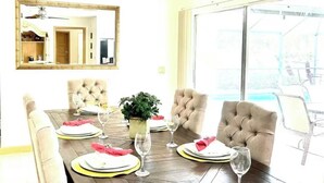Un comedor con una mesa de madera dispuesta para cuatro personas, rodeada de sillas acolchadas. Un espejo grande cuelga en la pared y hay una planta en maceta sobre la mesa.