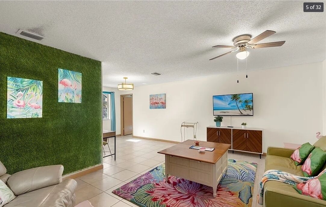 Un salon moderne avec un mur vert, un ventilateur de plafond, un téléviseur à écran plat et un coin repas comprenant une table et des chaises.