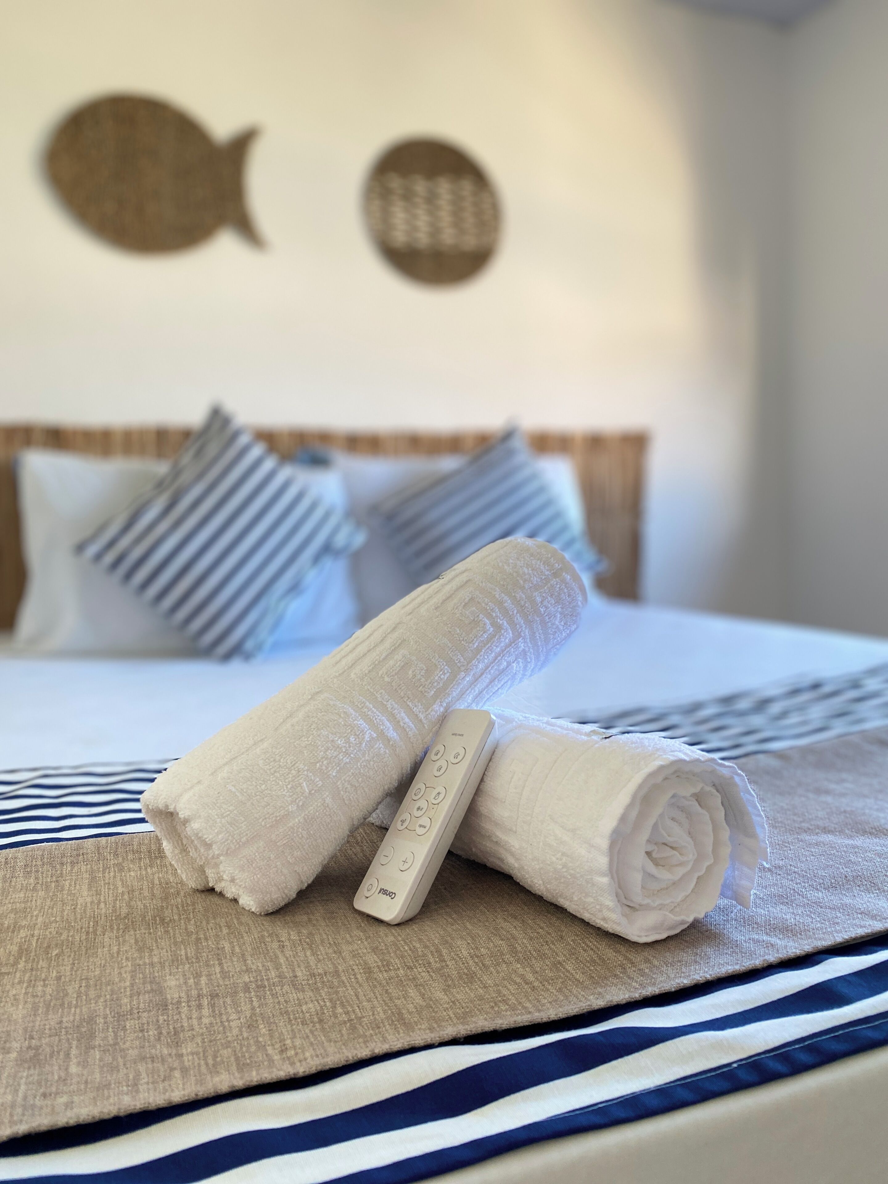 Cama bem arrumada com roupa de cama listrada, toalha enrolada e controle remoto sobre a cama.