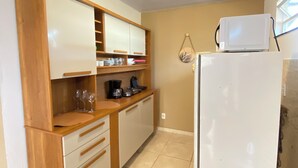 Eine kleine Küche mit Holzausstattung, einem weißen Kühlschrank und einer Mikrowelle darüber.