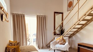 Ein geräumiges Zimmer mit einem großen Bett, einem Sessel, einer Treppe und einer Pendelleuchte.
