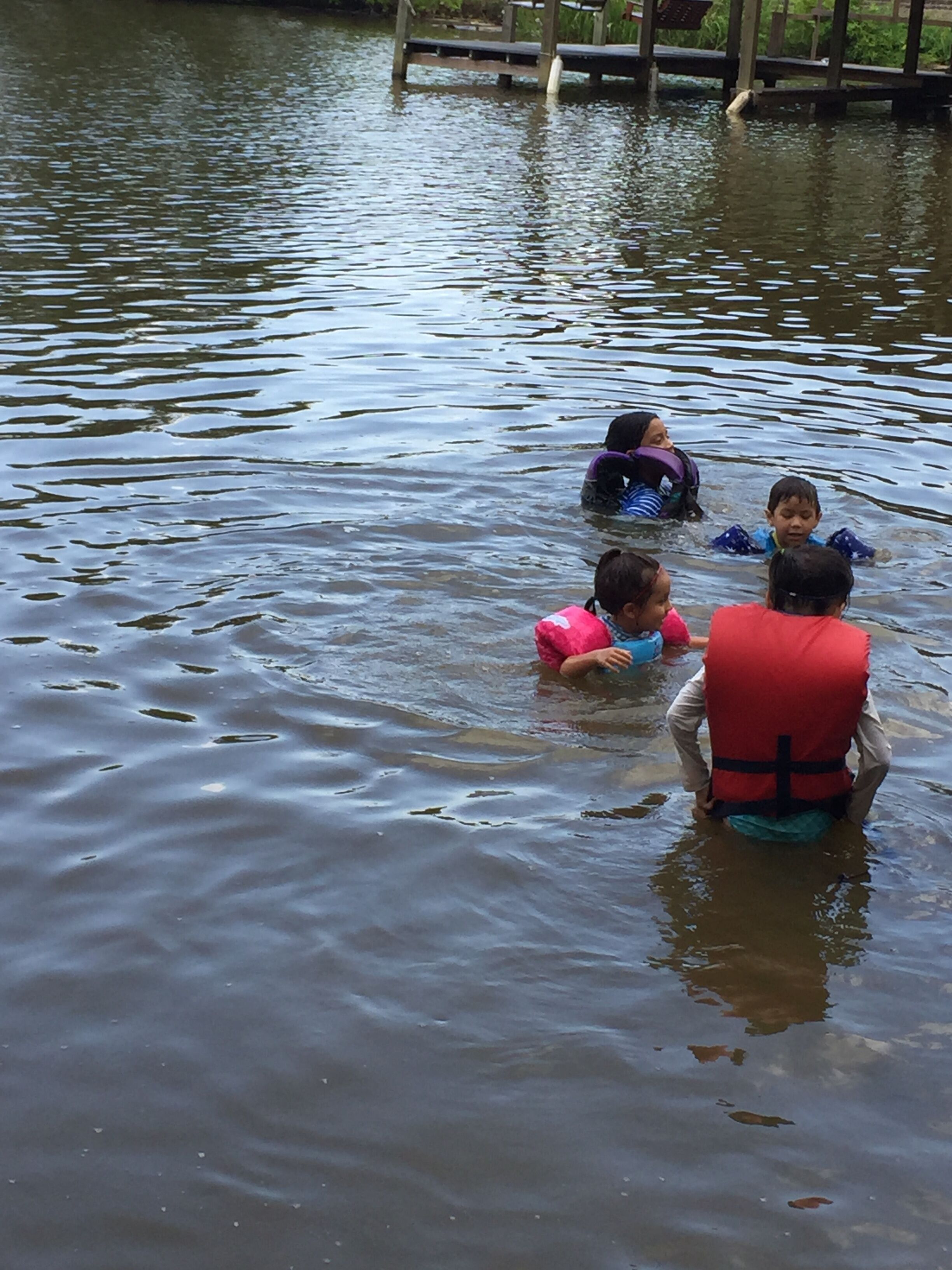 A group of children in a body of water, some wearing life jackets.