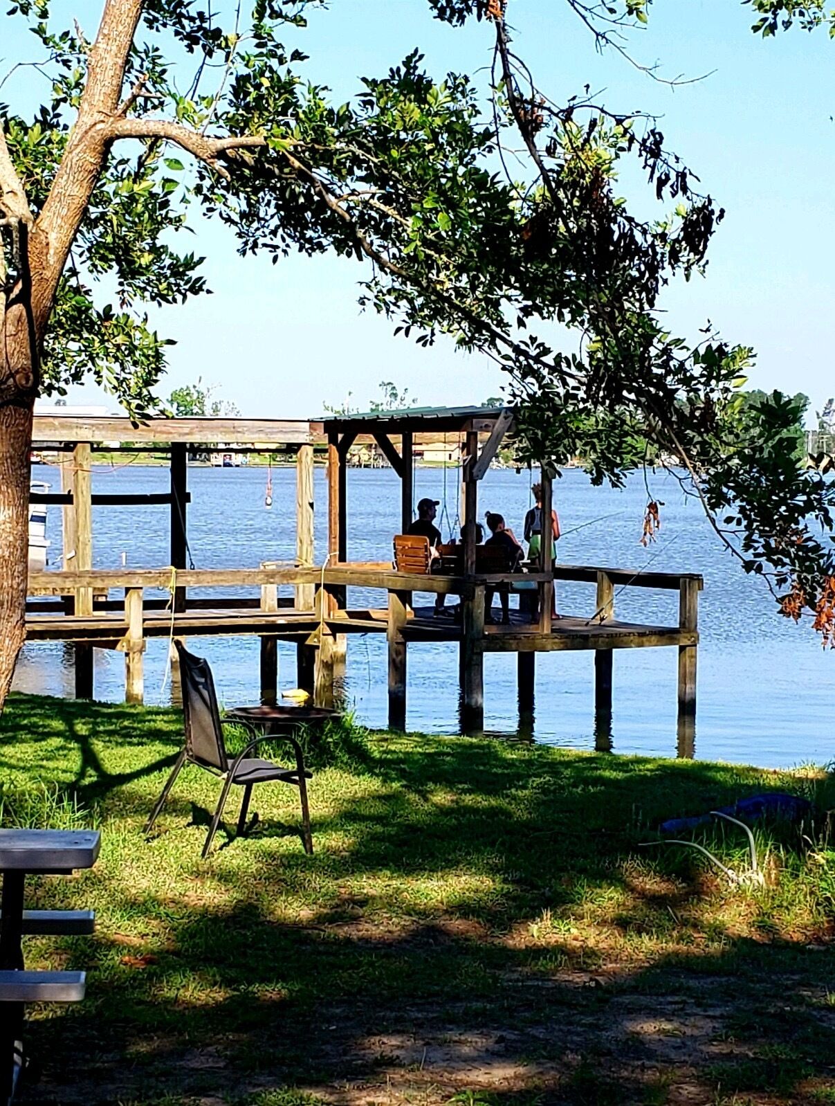 A wooden dock extending into a body of water, with a grassy area and a bench nearby.