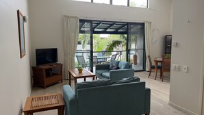 Een woonkamer met een bank, tv en een tafel. Er is een schuifdeur naar een buitenruimte met een tafel en stoelen.