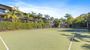 Een tennisbaan met een net, omringd door palmbomen en een gebouw met balkons.